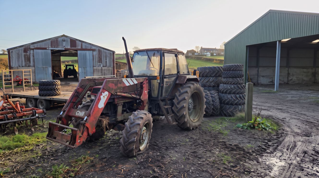 Tractor and stacked agricultural tyres in a farmyard