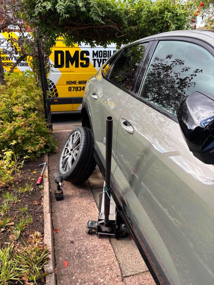 Car jacked up on a driveway with the wheel off during a mobile tyre fit