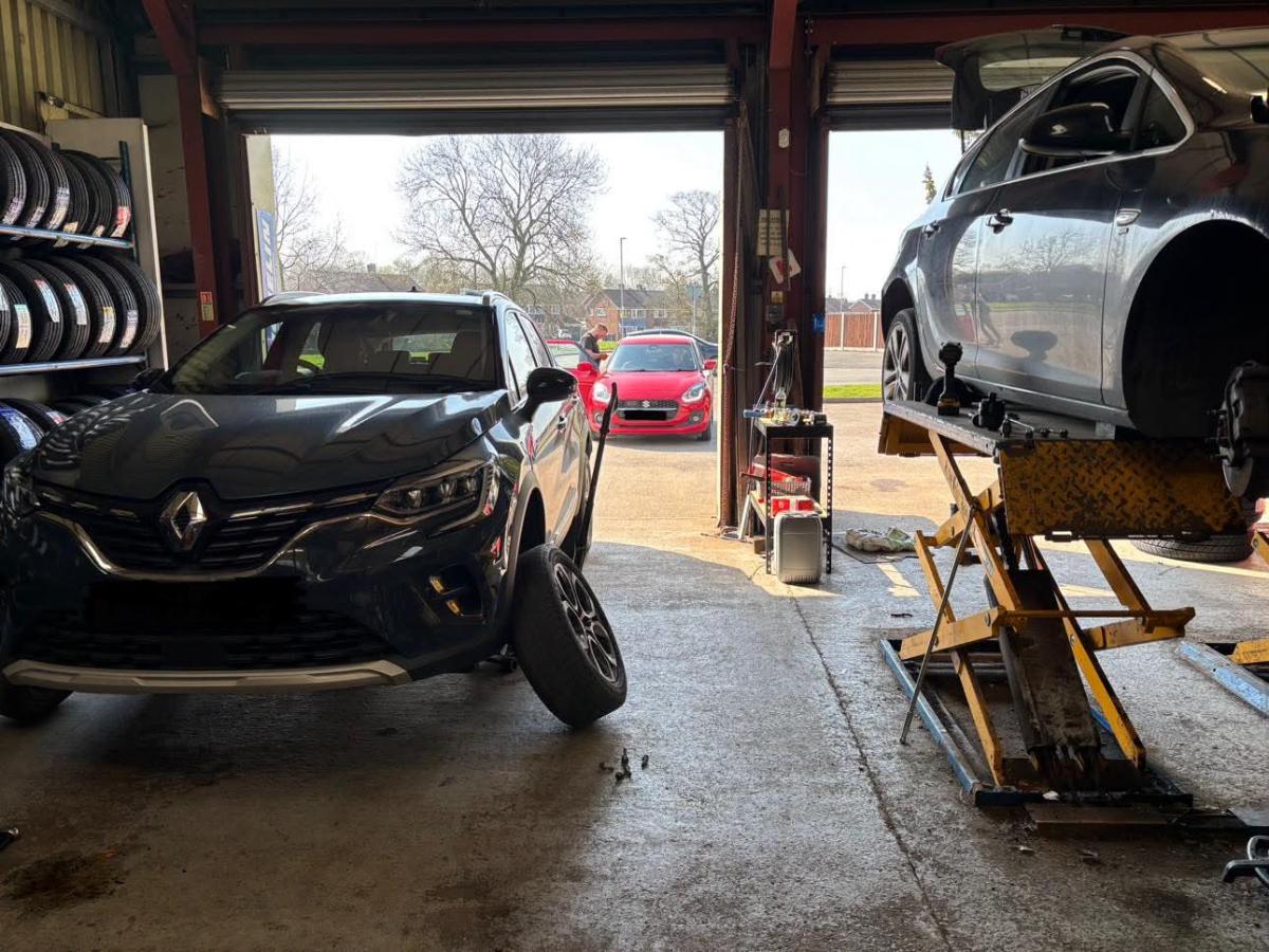 Cars being worked on in the DMS Tyres workshop at Blythe Bridge, one raised on a ramp beside racked tyres